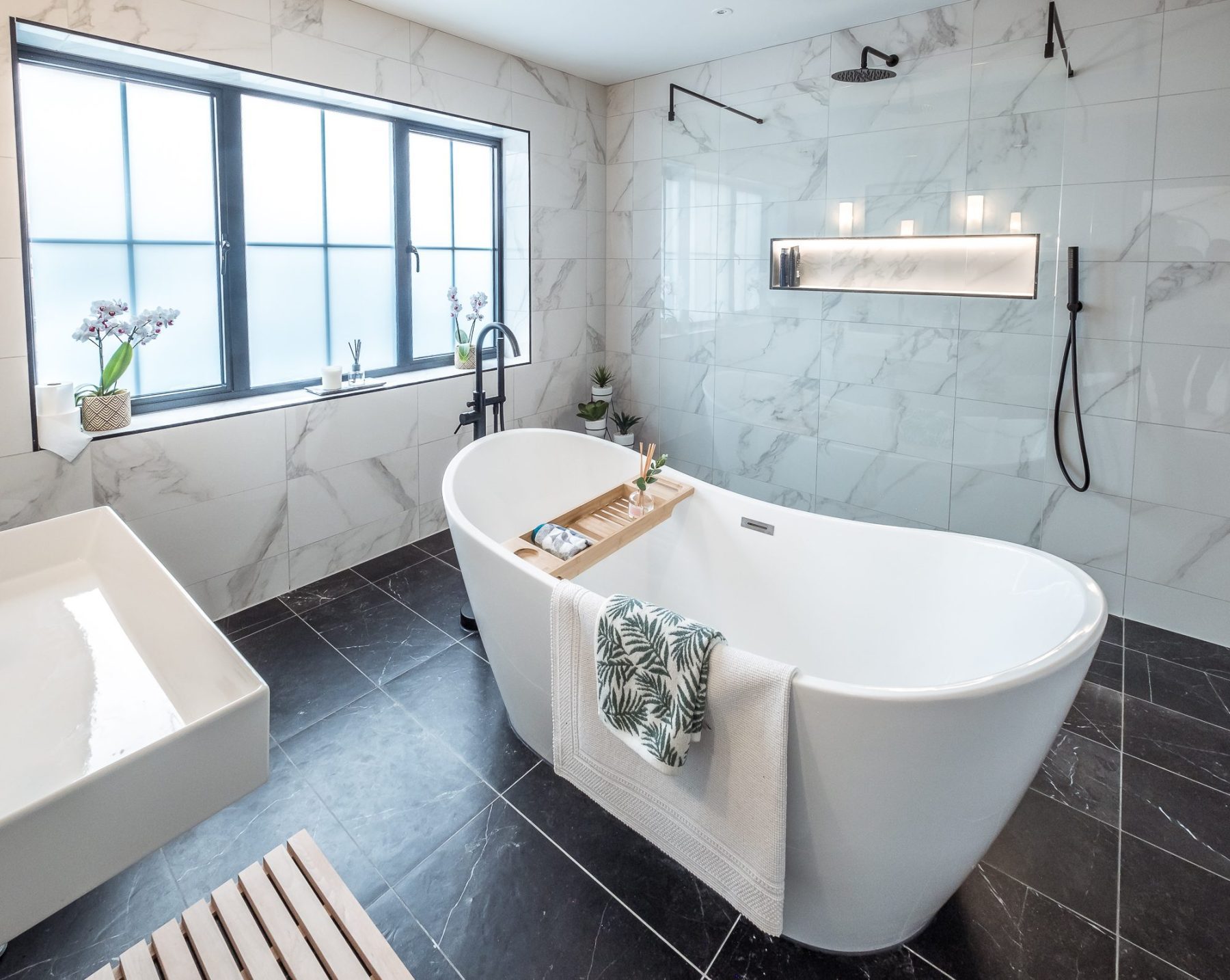 An internal view of the family bathroom with a free standing bath next to a large walk-in shower separated by a glass screen.