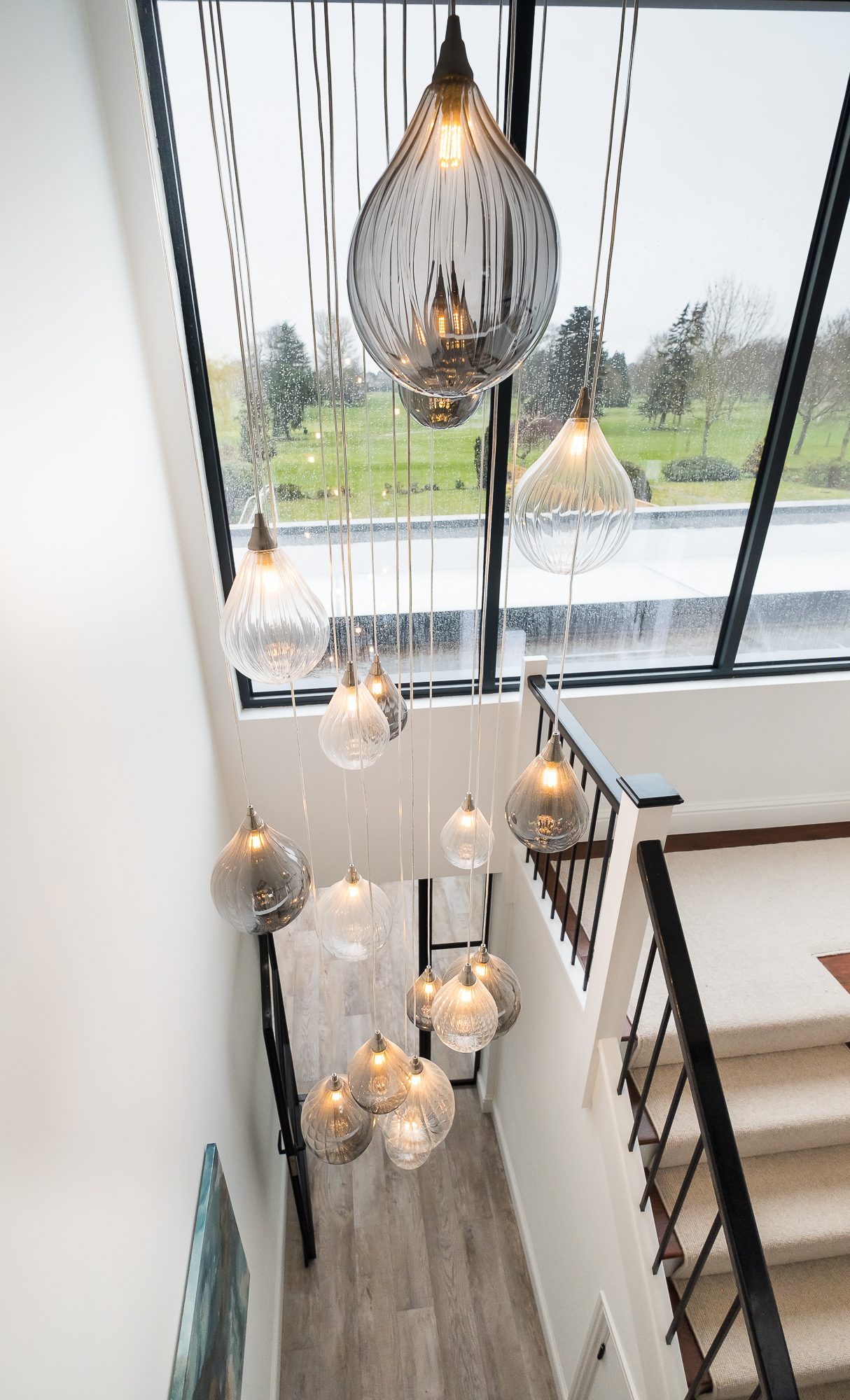 An internal view of the double height entrance hallway, looking down from the galleried landing at Topsham Road, with large windows looking across Exeter Golf and Country Club in the background.