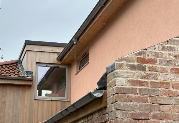 A close up external view of the exposed brick in the foreground with the contrasting vertical timber cladding and coloured render in the background at 2 Jays in Lympstone.